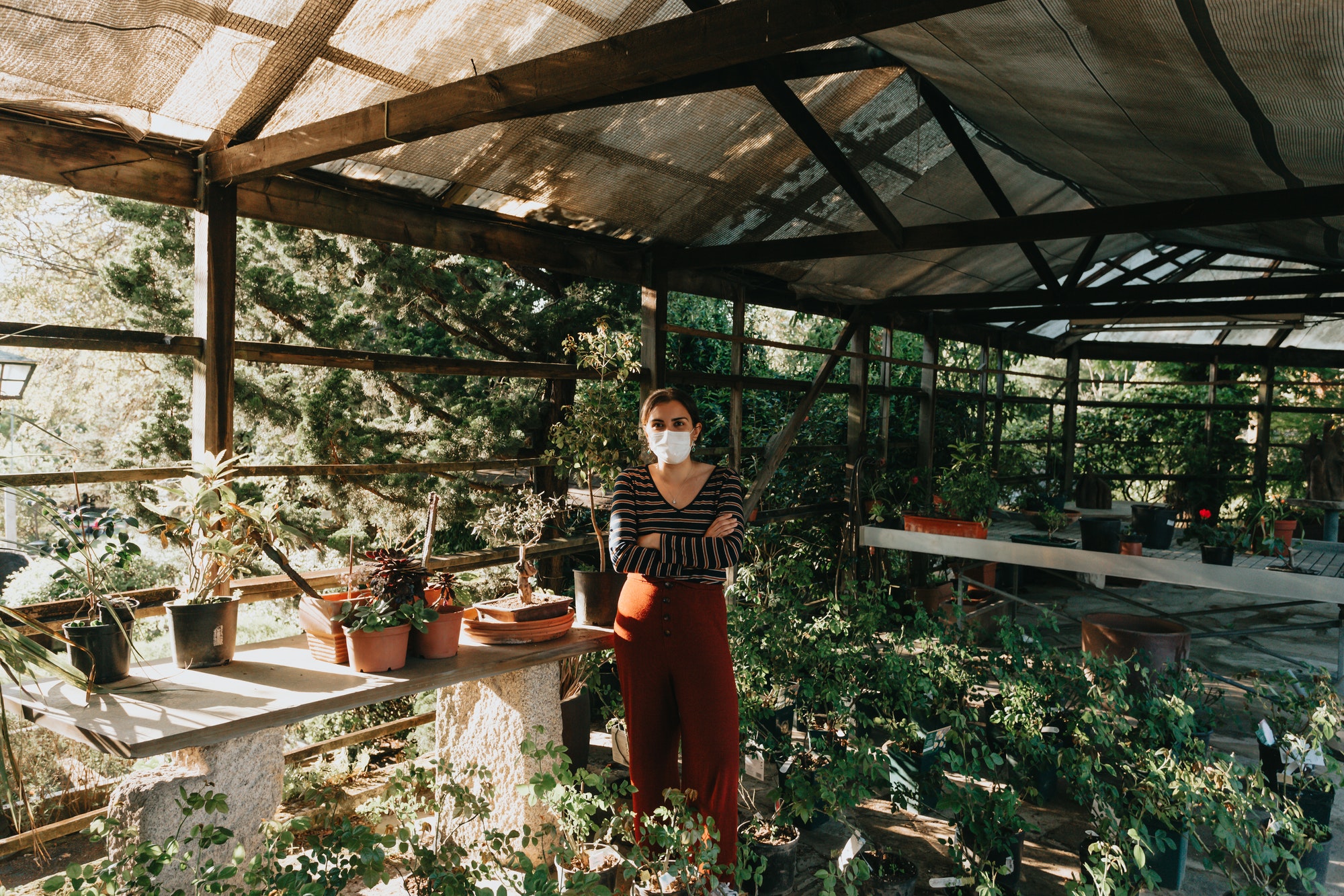 A woman wearing a mask doing some gardening during a super sunset, with a lot of plants